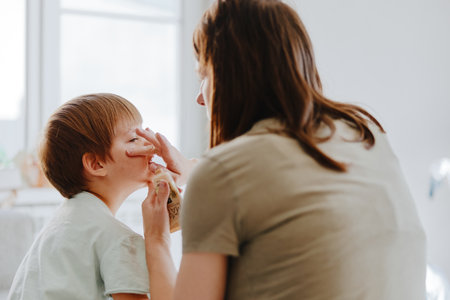 Caring woman applying makeup on a child, showcasing a tender moment of bonding and creativity. The warm atmosphere evokes a sense of joy and innocence.の写真素材