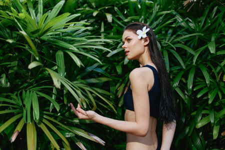 Exotic Asian Woman in Stylish Black Swimsuit Poses in Front of Vibrant Green Foliageの写真素材