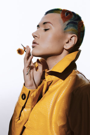 woman with colorful shaved hairstyle wearing a vibrant yellow leather jacket, posing thoughtfully with closed eyes against a simple white background, stylish and modern fashionの写真素材