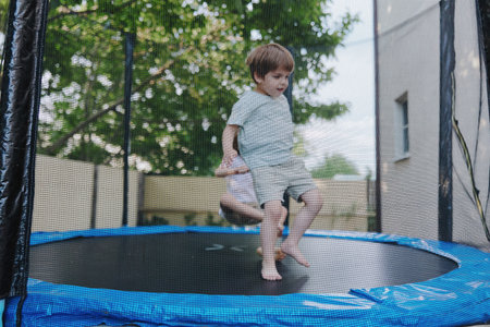 Happy boy bouncing on a trampoline, enjoying outdoor playtime, vibrant summer atmosphere, and playful energy radiating in a sunny setting.の写真素材