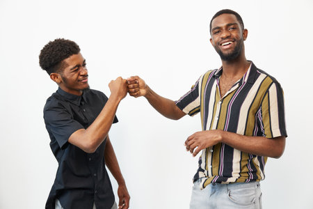 Black men sharing a joyful moment with a fist bump, showcasing friendship and camaraderie in a bright, cheerful atmosphere.の写真素材