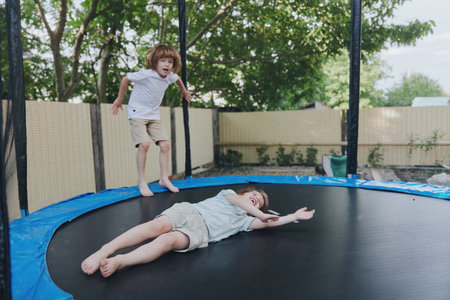 Playful boys jumping on a trampoline, enjoying a sunny day outdoors. Their laughter and excitement fill the air, creating a joyful atmosphere of childhood play.の写真素材