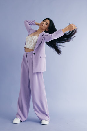 young woman in a lilac suit and white top posing with flowing black hair against a soft blue background, stylish, dynamic, modern look, fashion outfitの写真素材