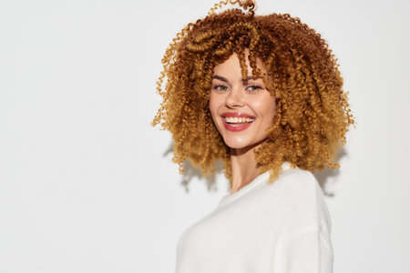 Smiling young woman with curly hair on a light background, exuding joy and confidence, showcasing natural beauty and youthful charmの写真素材