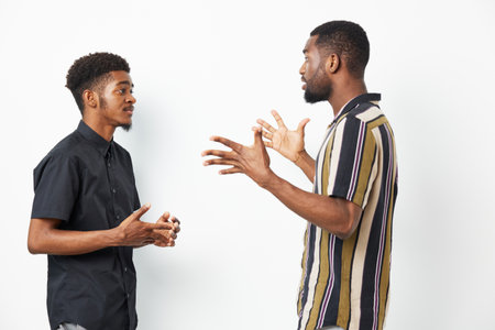 Two black men engaging in an animated conversation, showcasing expressions of interest and enthusiasm, wearing casual attire in a bright setting.の写真素材