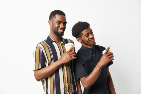 Two black men enjoying coffee together, sharing smiles and laughter, dressed casually in stylish...