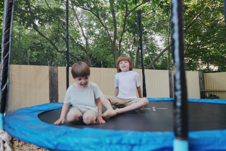 Happy children jumping on a trampoline, enjoying a sunny day outdoors, surrounded by greenery and laughter, experiencing the joy of play.の写真素材