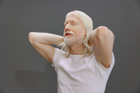 Elderly man relaxing with white hair and beard against a gray background, conveying calmness and serenity, showcasing the beauty of aging and self acceptance, with a peaceful expressionの写真素材