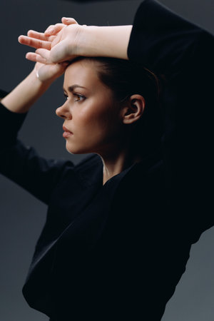 thoughtful woman posing with raised arms in black clothing against dark background, showing a calm and focused expression in soft lightingの写真素材