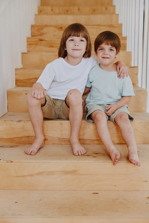 Two smiling boys sit on wooden stairs, showcasing a cheerful moment of friendship and playfulness with natural, warm lighting.の写真素材