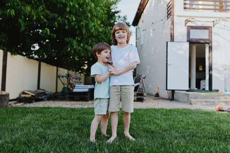 Two cheerful boys standing outdoors in a sunny garden, enjoying each others company and playing. Their joy and innocence are palpable in this vibrant scene.の写真素材