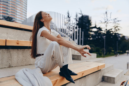 woman enjoying peaceful moment outdoors sitting on wooden steps in casual white outfit smiling with eyes closed KEY: woman, peaceful, outdoors, casual, white, smiling, relaxation, sitting, steps, joy, happiness, casualwear, lifestyle, summer, freshair, nature, urban, young, female, serene, calm, happiness, beauty, tranquility, lifestyle, leisure, weekend, casualstyle, happiness, freedom, natural, expression, happiness, calmness, contentment, peacefulness, positive, bright, carefree, fashion, style, confident, fresh, springの写真素材