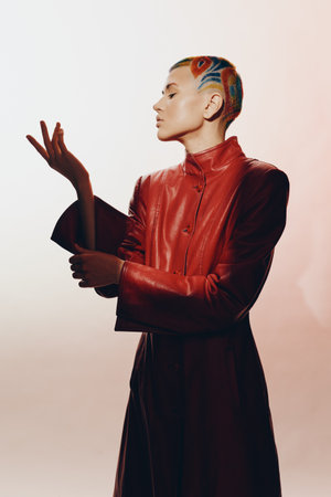 Profile of a woman with colorful shaved hair wearing a long red leather coat, posing with elegance against a minimalist light background, modern fashion expression.の写真素材