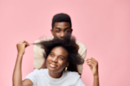 A joyful African couple embracing each other s hairstyles, with a soft pink background, showcasing beautiful natural hair and playful emotionsの写真素材