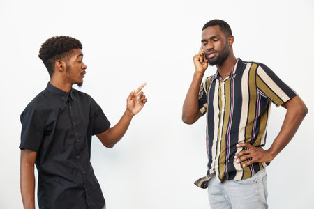 Two African American men engaged in a conversation, one gesturing animatedly while the other is on a phone call. Their expressions reflect a lively discussion.の写真素材