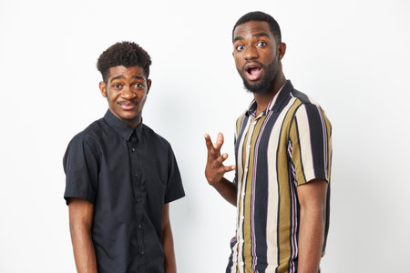 Two black men express surprise and joy with their playful poses against a neutral background. Their...