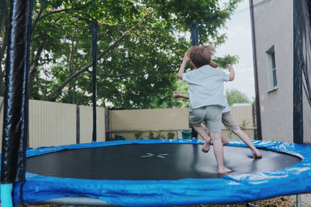 Joyful children playing on a trampoline, enjoying their carefree day outdoors surrounded by greenery...