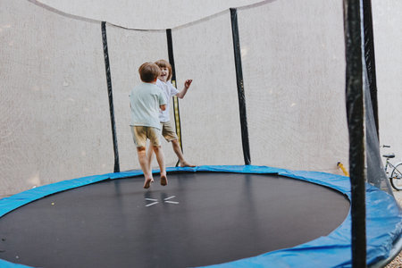 Two happy children jumping on a trampoline, enjoying outdoor play in a sunny setting, showcasing joyful moments and energetic fun.の写真素材