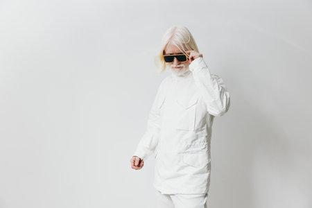Fashionable elderly person in white outfit and sunglasses on plain background, showcasing modern style and confidence Unique aesthetic with a cool vibe, capturing individuality and flairの写真素材