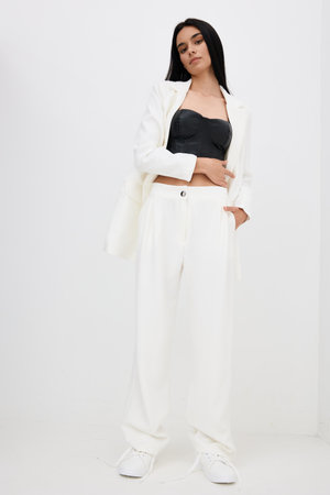 woman in white suit and black top standing confidently in minimalistic studio with neutral background, wearing white sneakers, relaxed pose, modern fashion styleの写真素材