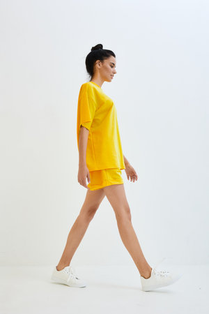 Woman walking confidently in bright yellow casual outfit against white background, showcasing sporty style and relaxed mood in vibrant color palette.の写真素材