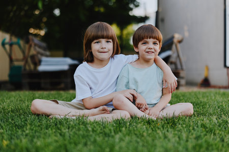 Two smiling boys enjoy a sunny day outdoors, sitting together on grass, dressed casually. Their cheerful expressions reflect happiness and friendship.の写真素材
