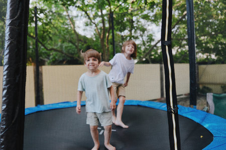 Happy children playing on a trampoline, enjoying a sunny day outdoors with greenery in the background and vibrant colors around them.の写真素材