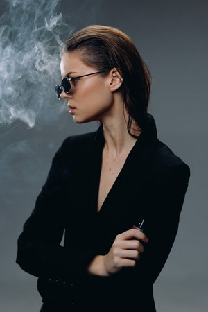 stylish woman wearing sunglasses smoking electronic cigarette with smoke, teenage, black clothing,...