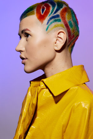 Woman with colorful shaved hair in a yellow jacket, showing artistic style and unique fashion against a soft purple background, capturing modern creativity and boldness.の写真素材