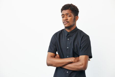 Confident black man with crossed arms, wearing a sleek black shirt against a plain background. Ideal...