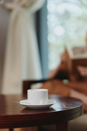 Relaxing moment with a cup of coffee on a wooden table by a window, showcasing tranquility, indoor lifestyle, and a warm atmosphere with soft natural lightの写真素材