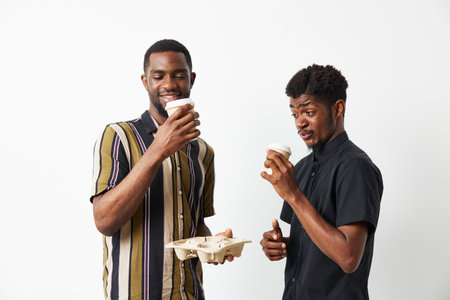 Two smiling African American men enjoy coffee together, showcasing friendship and joy. Their stylish outfits highlight a contemporary urban vibe.の写真素材