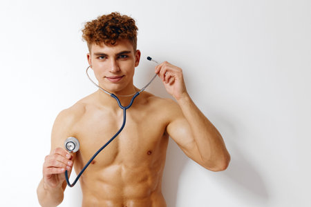 Confident young man with curly hair holding stethoscope, smiling at the camera. Health and wellness concept with a focus on fitness and medical profession.の写真素材