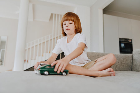 Young boy playing with toy cars, sitting on a cozy sofa in a modern living room, showcasing imagination and creativity in a relaxed environment.の写真素材