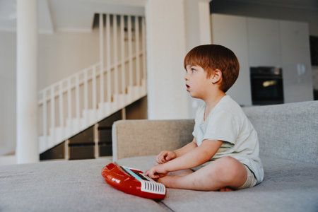 Curious boy playing with a toy keyboard, focused expression and casual attire, indoor setting with soft lighting, creating a warm atmosphere.の写真素材