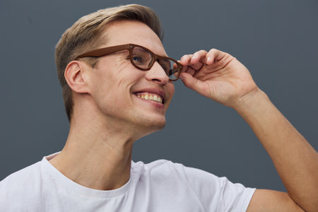 Smiling man with glasses adjusting his eyewear, wearing a white t-shirt, cheerful expression, studio...