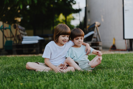 Happy children sitting together on grass, enjoying a sunny day in the park, sharing laughter and playful moments with friends outside.の写真素材