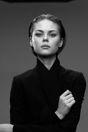 Black and white portrait of a serious woman with wet hair wearing a dark outfit, displaying confidence and elegance in a studio setting with a plain background.の写真素材