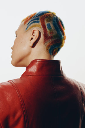 Woman with colorful short hair design and shaved patterns, wearing red leather jacket, seen from behind against white background, creative modern style.の写真素材