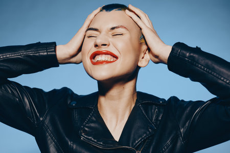 Young woman with shaved head and bright red lipstick smiling joyfully, wearing a black leather...