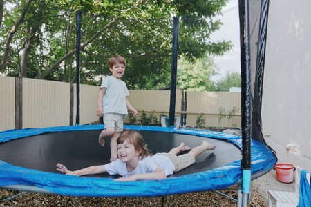 Happy children playing on a trampoline, enjoying outdoor fun and laughter in a sunny backyard setting filled with greenery and joy.の写真素材