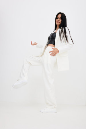woman in white suit posing confidently with black top and sneakers in bright studio, showcasing modern fashion style with dynamic posture and casual eleganceの写真素材