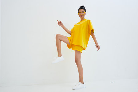 smiling woman in bright yellow casual outfit poses energetically against white background, wearing matching shorts and sneakers with cheerful expressionの写真素材