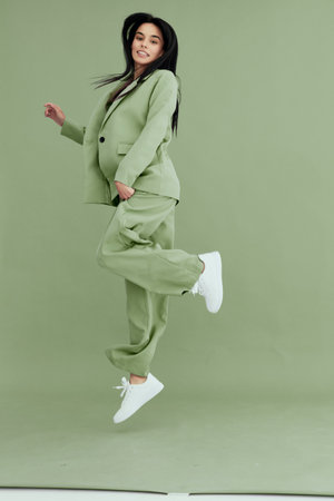 young woman jumping in green suit with white sneakers, smiling, energetic and joyful, isolated on...