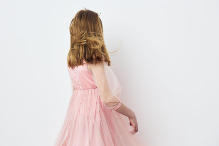 A young girl in a pink tulle dress with flowing hair, expressing joy while facing away against a clean white background, ideal for children s fashion and happiness conceptsの写真素材