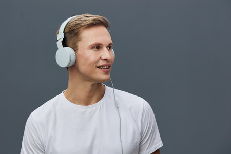 Smiling young caucasian man wear headphones listen music casual white t-shirt isolated gray...
