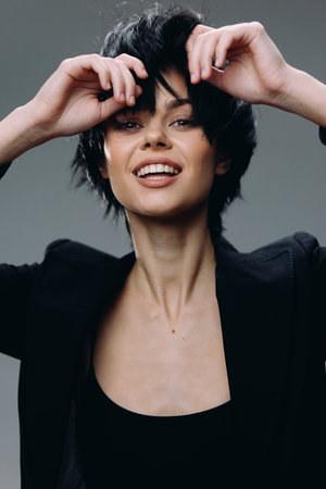 smiling woman with short black hair wearing black blazer and top, joyful expression, studio background, young adult European ethnicity, casual styleの写真素材