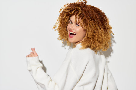 Happy woman with curly hair smiling on a bright white background, wearing a cozy oversized sweater Joyful expression, youthful vibe, perfect for lifestyle and fashion themesの写真素材