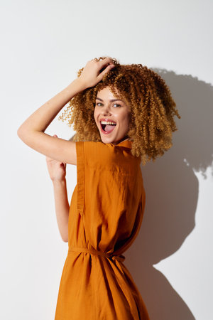 Happy woman with curly hair in orange outfit poses against a white background, showcasing joy and...
