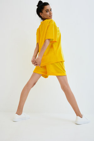 Young woman stretching in vibrant yellow sportswear and white sneakers against a plain white background, showcasing fitness and casual style in bright colors.の写真素材